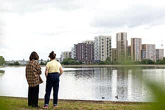 Two people looking out at the water at Walthamstow Wetlands with city buildings in the distance.